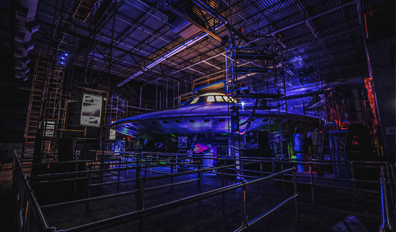 A disc-like structure in the middle of a room, surrounded by scaffolding and metal queue bars