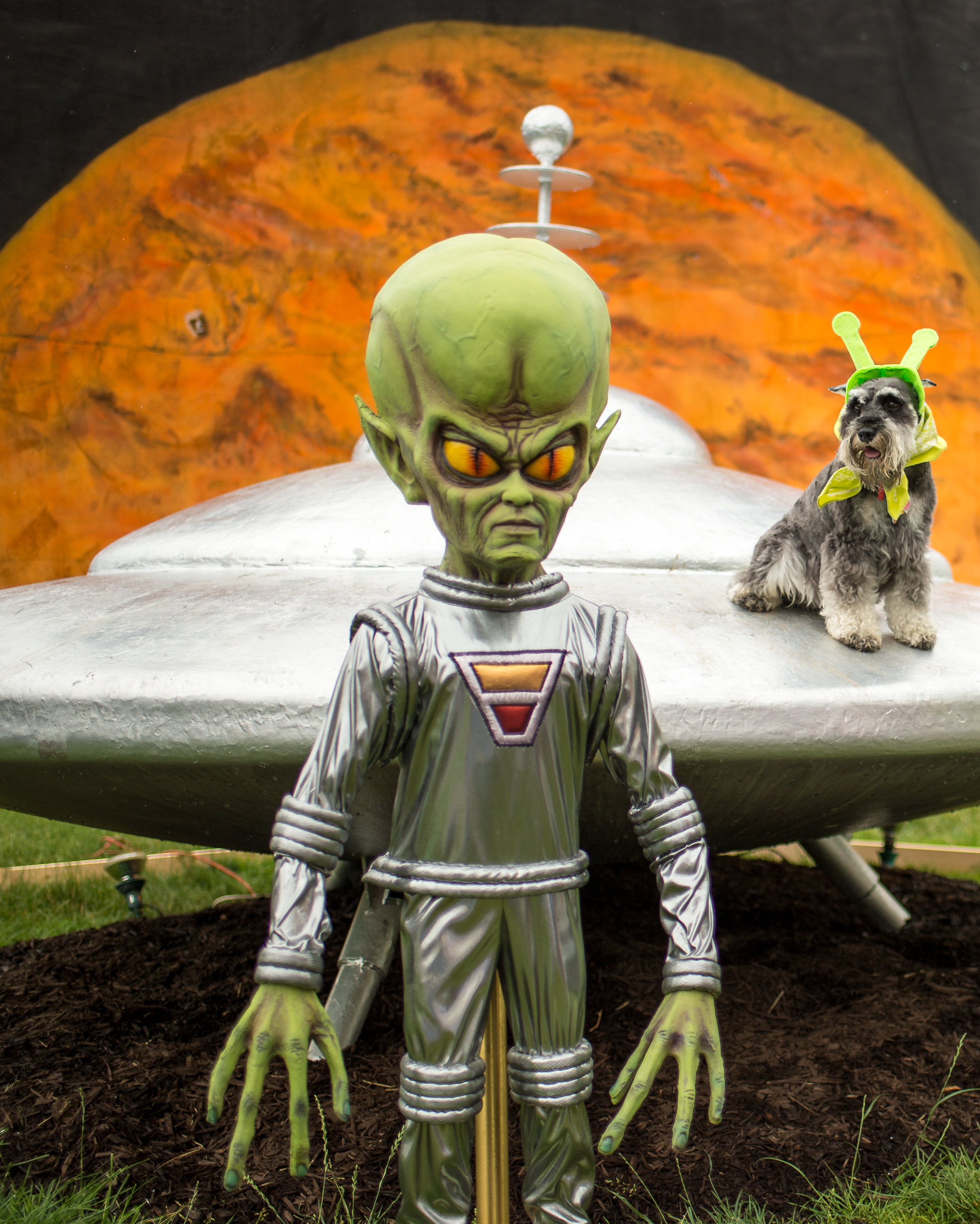 Green alien-like being in front of a silver object meant to be an unidentifiable flying object
