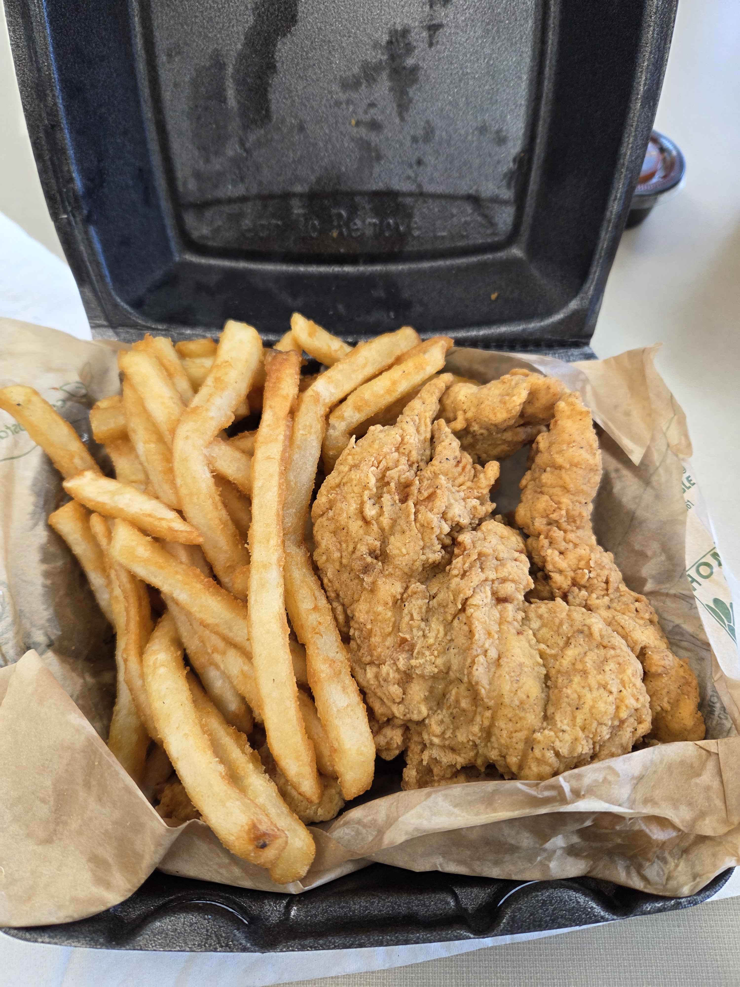 Image of chicken tenders and fries in a black take out box.