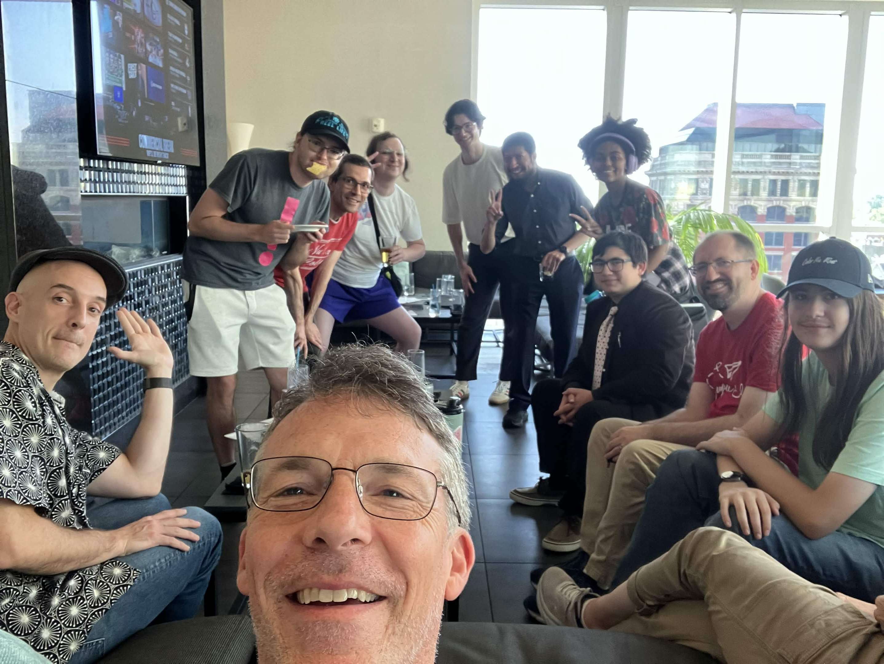 Group of people in front of large windows and a wall-mounted tv.